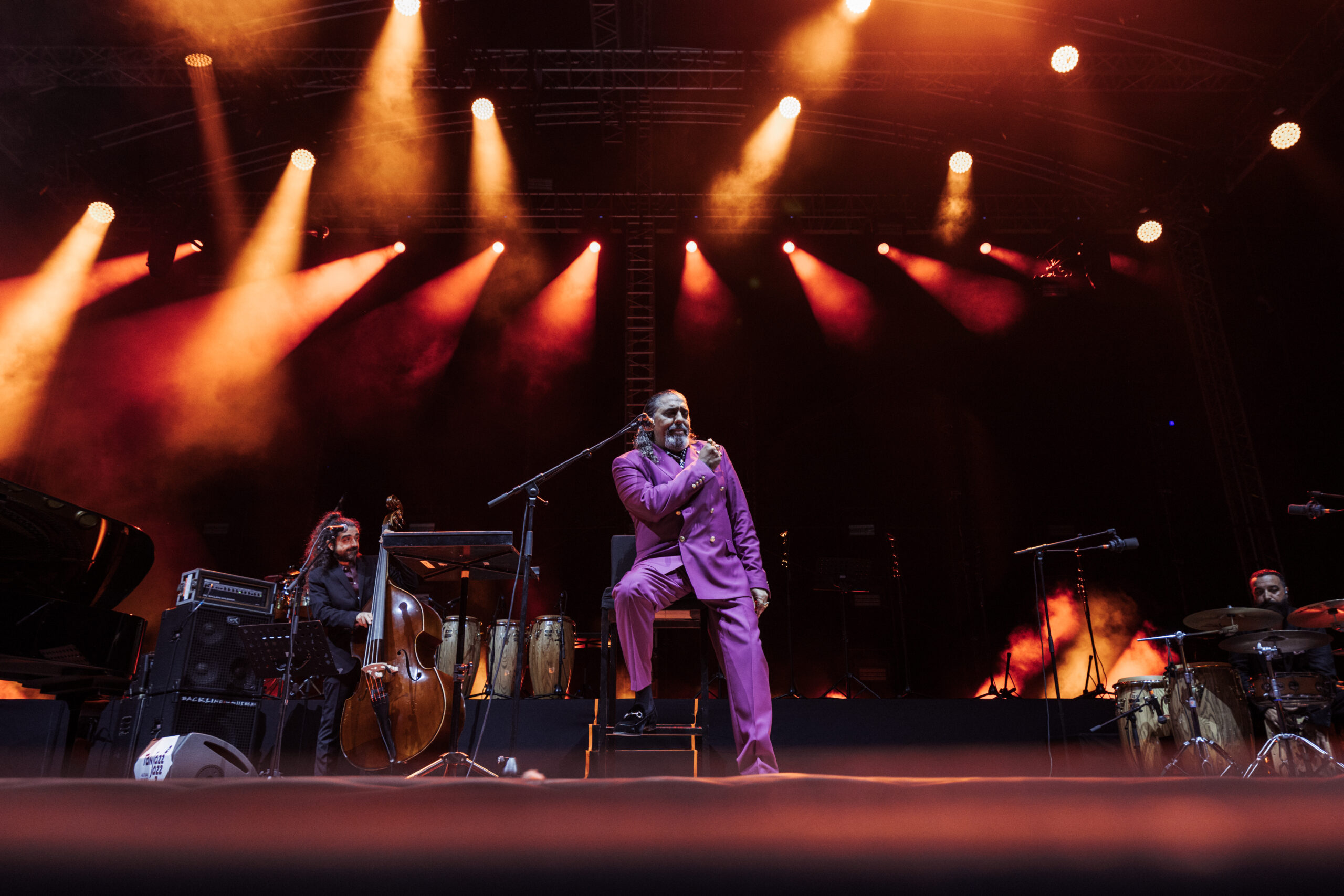 Diego El Cigala cantando sentado con el contrabajo y la percusión en el escenario