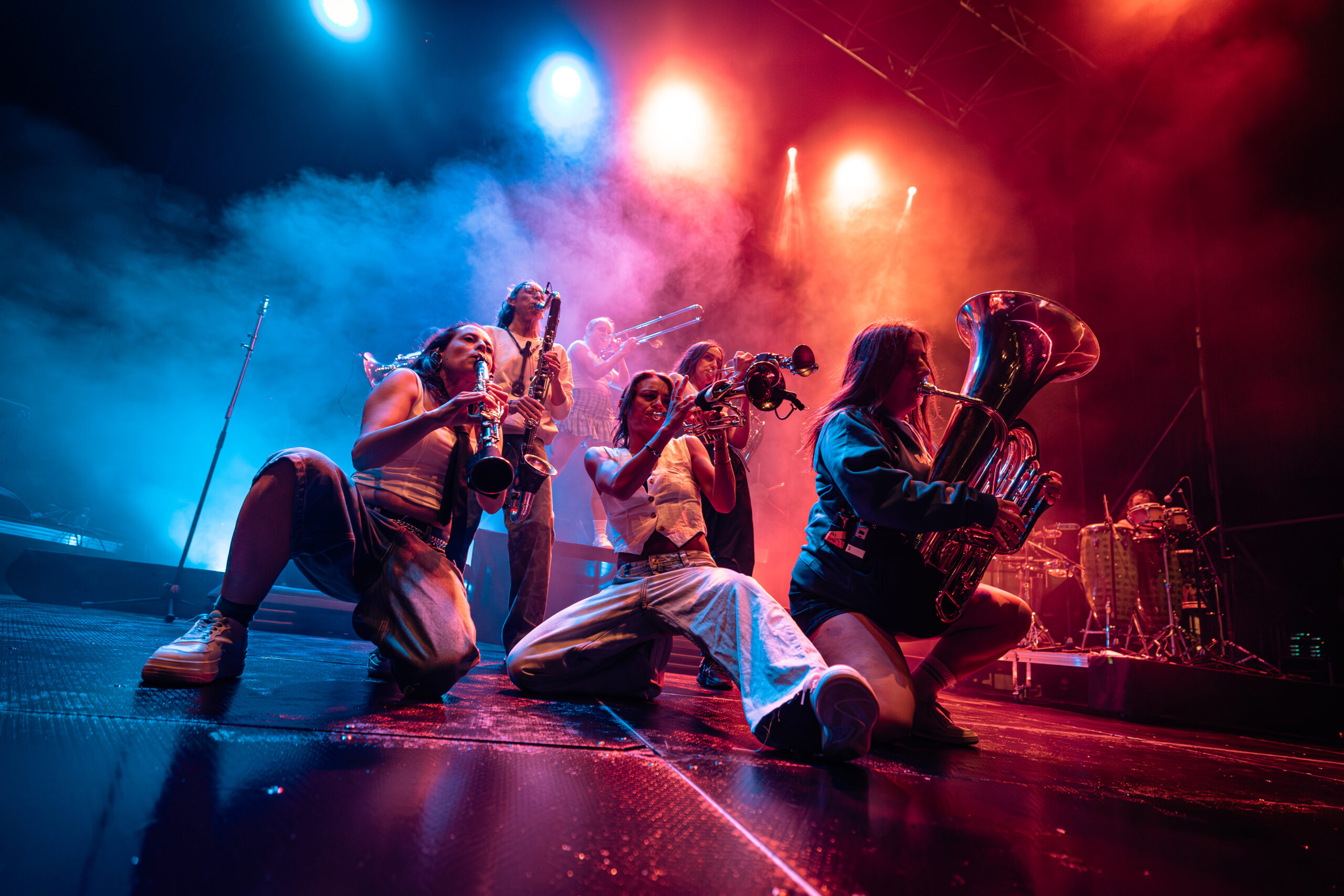 Sección de metales de rodillas en el escenario del WOMAD bajo luz azul y roja