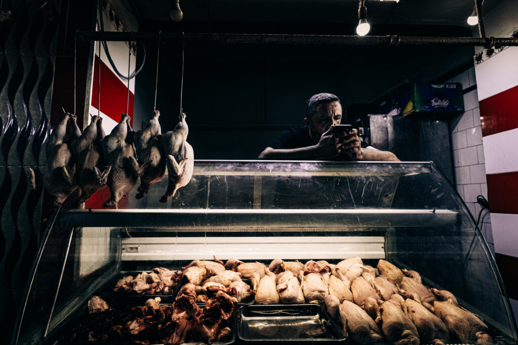 Carnicero del mercado de Tánger tras el mostrador, con aves colgadas en primer plano